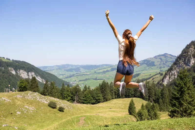A woman is jumping in the air on top of a grassy hill.