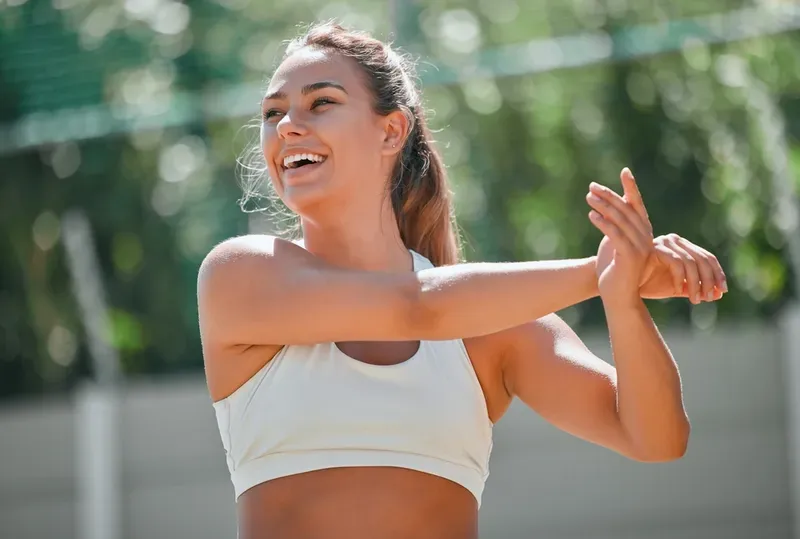 A woman in a white sports bra is stretching her arms.