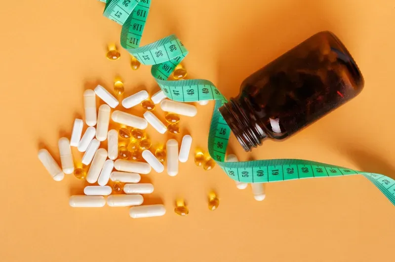 A bottle of pills spilling out of it next to a measuring tape.