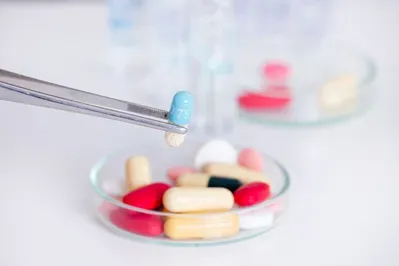 A person is taking a capsule out of a petri dish with tweezers.