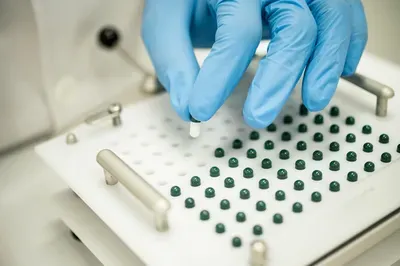 A person wearing blue gloves is putting a capsule into a machine.