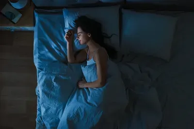 A woman is sleeping in a bed with blue sheets at night.