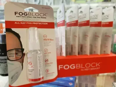 A man wearing glasses and a mask is standing next to a bottle of fogblock spray.