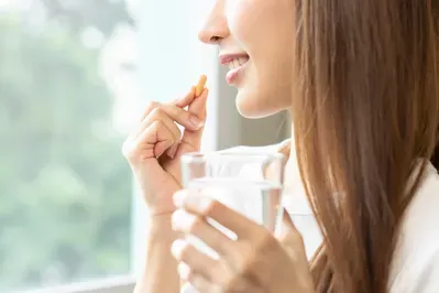 A woman is taking a pill from a glass of water.
