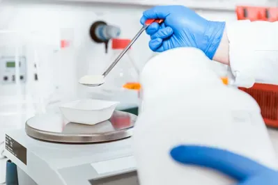 A person wearing blue gloves is measuring a substance on a scale.