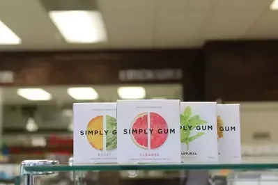 Three boxes of simply gum are sitting on a glass shelf.