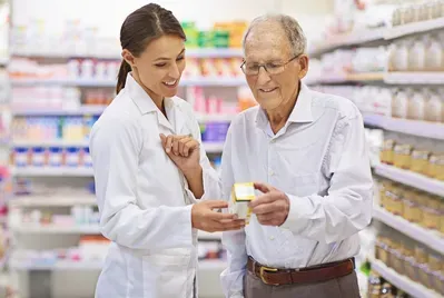 A female pharmacist is talking to an older man in a pharmacy.