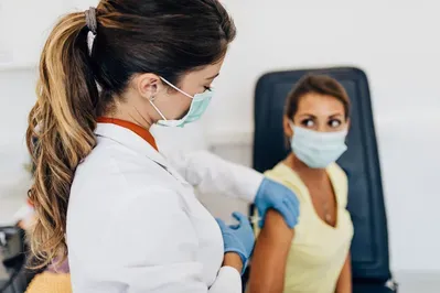 A woman wearing a mask is getting a vaccine from a doctor.