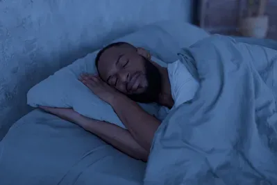A man is sleeping in a bed with a blue blanket.