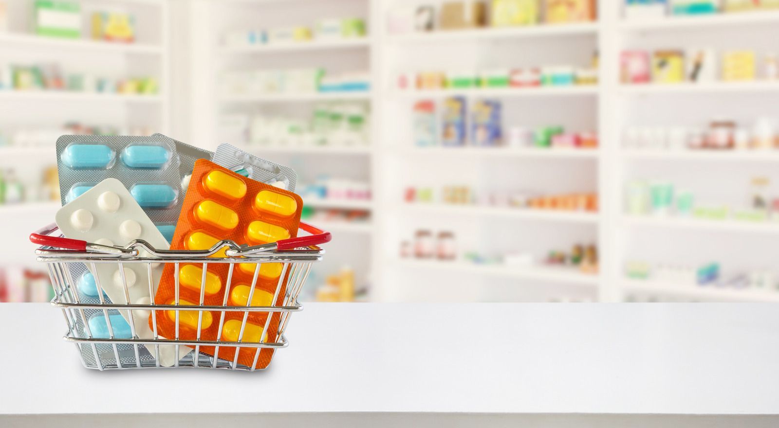 Medicine bottles, blister packs, and pills in a shopping basket on a pharmacy counter
