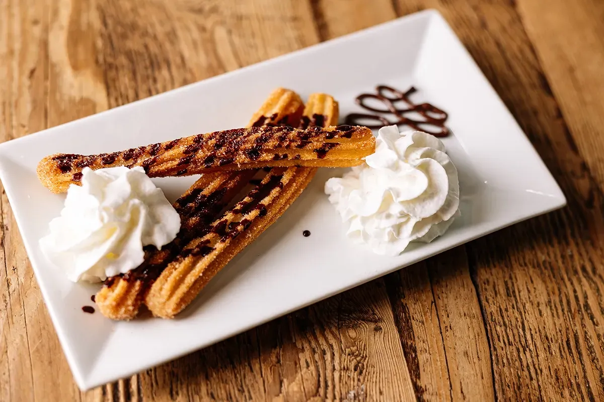 A white plate topped with churros and whipped cream on a wooden table.