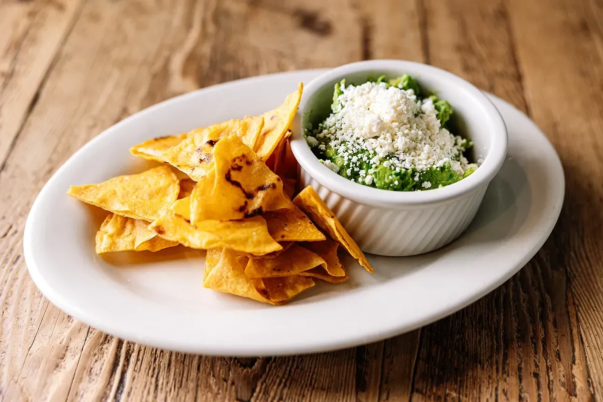 A white plate topped with tortilla chips and guacamole on a wooden table.
