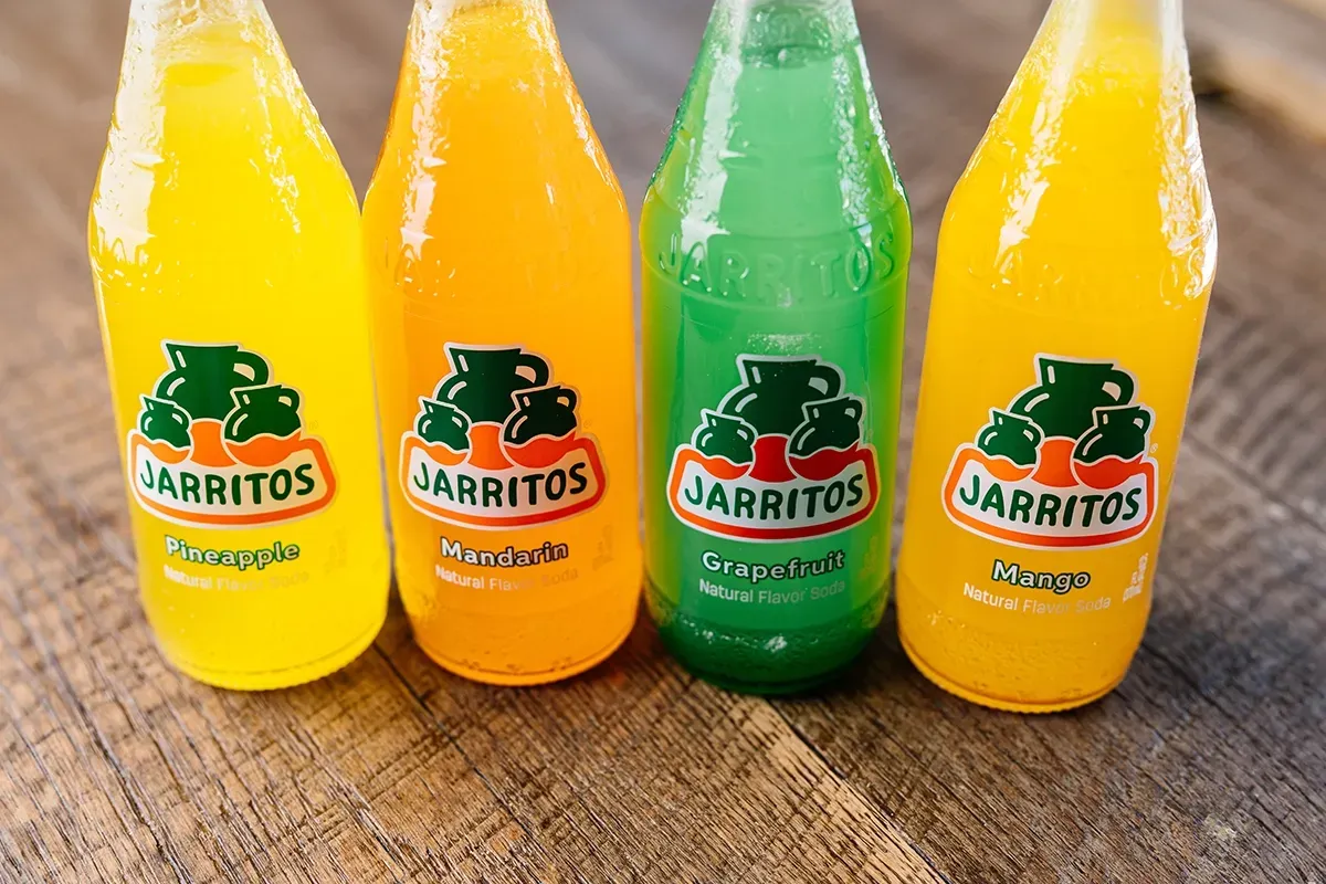 Four bottles of jarritos are lined up on a wooden table.