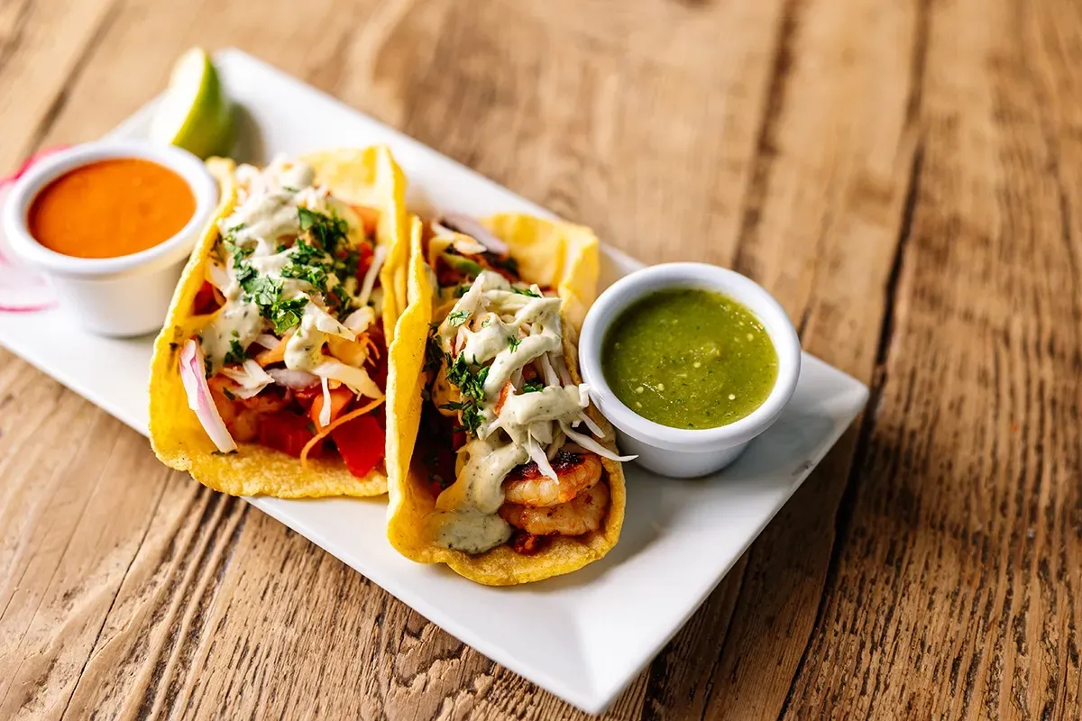Two tacos with sauces on a white plate on a wooden table.