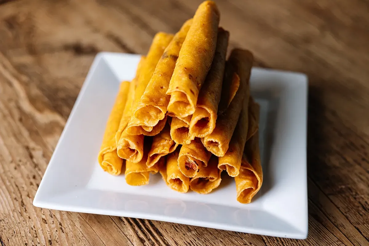 A white plate topped with a stack of taquitos on a wooden table.