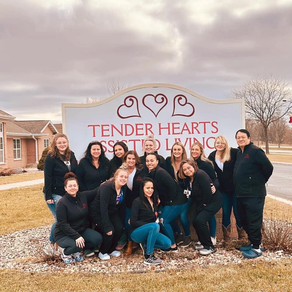 The Tender Hearts team is posing for a picture in front of a tender hearts sign.