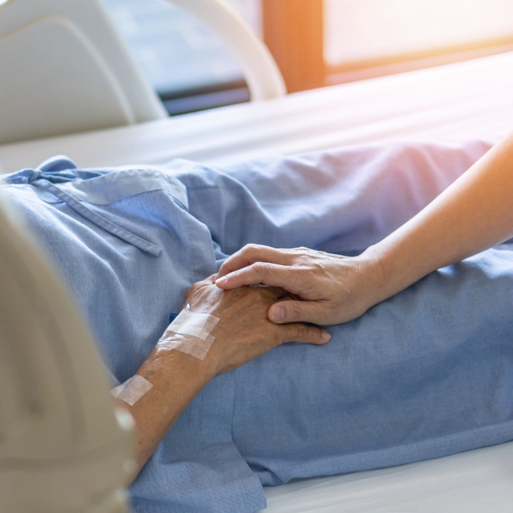 A person is laying in a hospital bed holding another person 's hand.