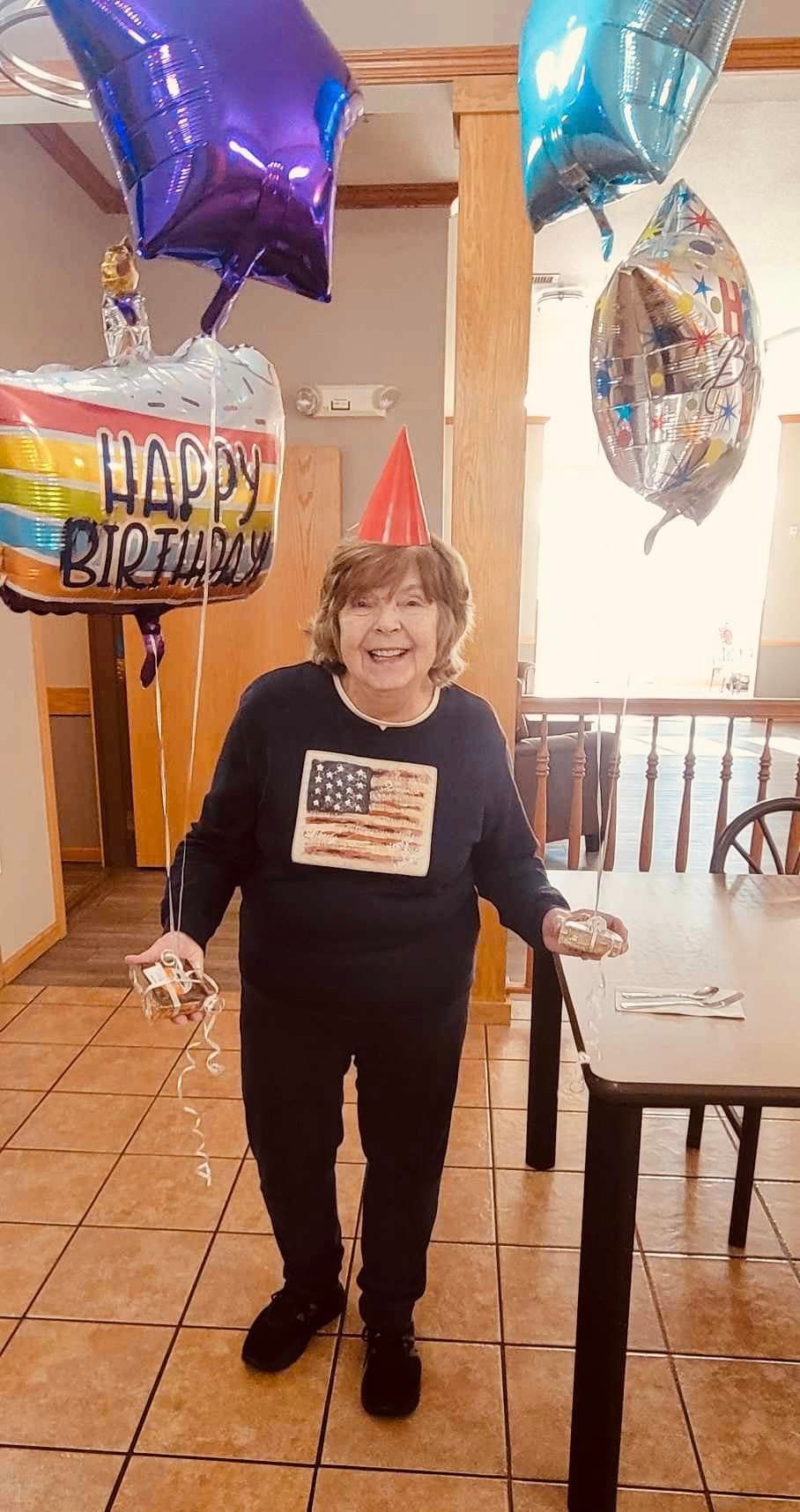 A woman is standing in a room with balloons and a happy birthday balloon.