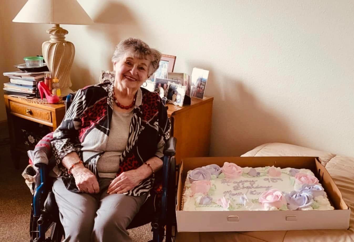 An elderly woman in a wheelchair is sitting next to a birthday cake