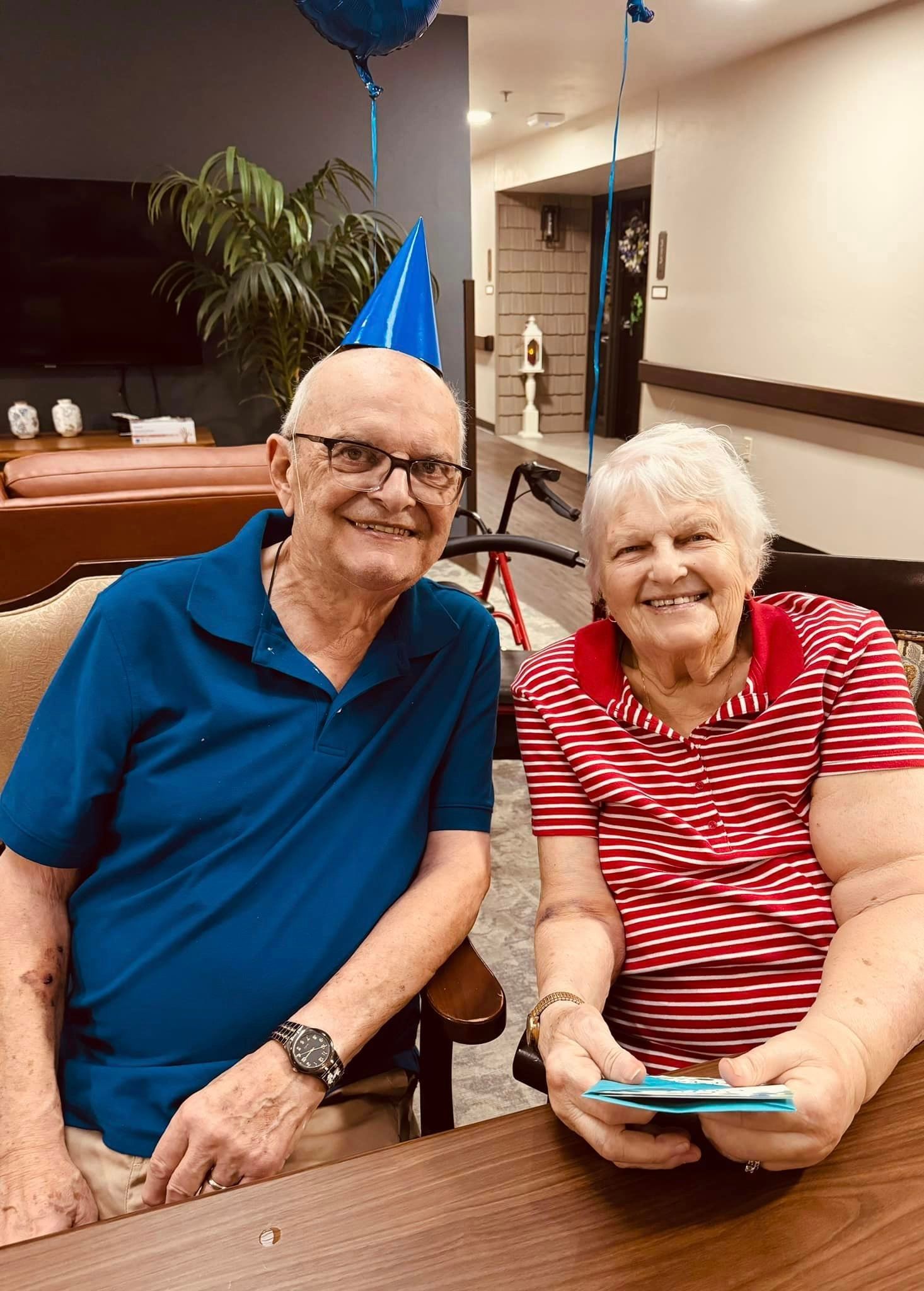 A man and a woman are sitting at a table with balloons in the background.