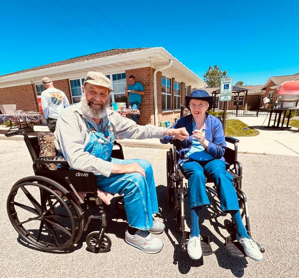 A man in overalls is sitting next to a woman in a wheelchair.
