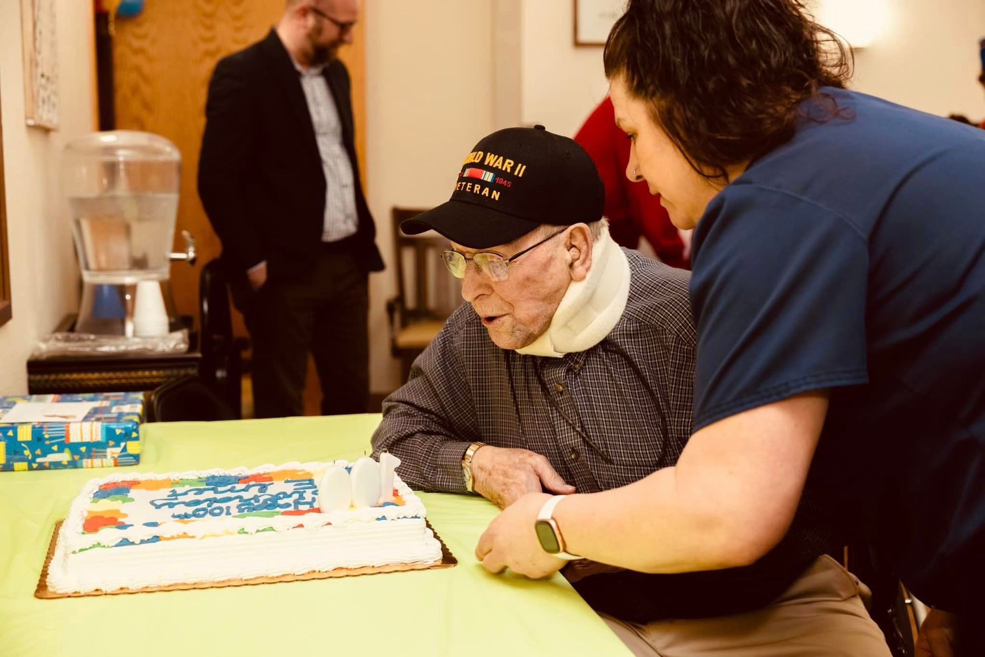 A woman is helping an elderly man cut a birthday cake.