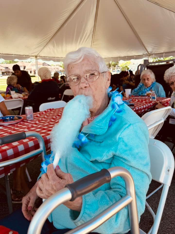 An elderly woman wearing glasses is sitting in a wheelchair and smiling.