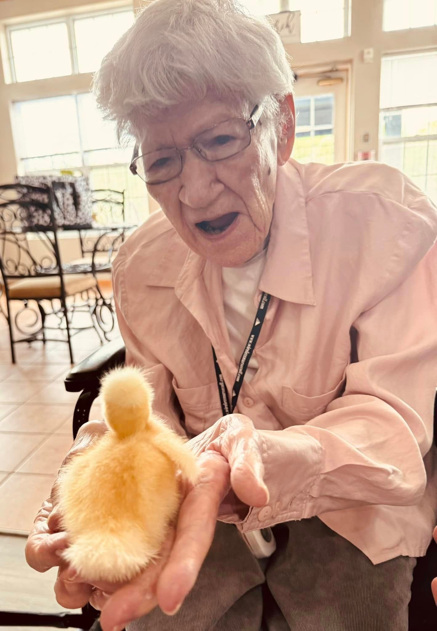 An elderly woman is holding a small duck in her hands.