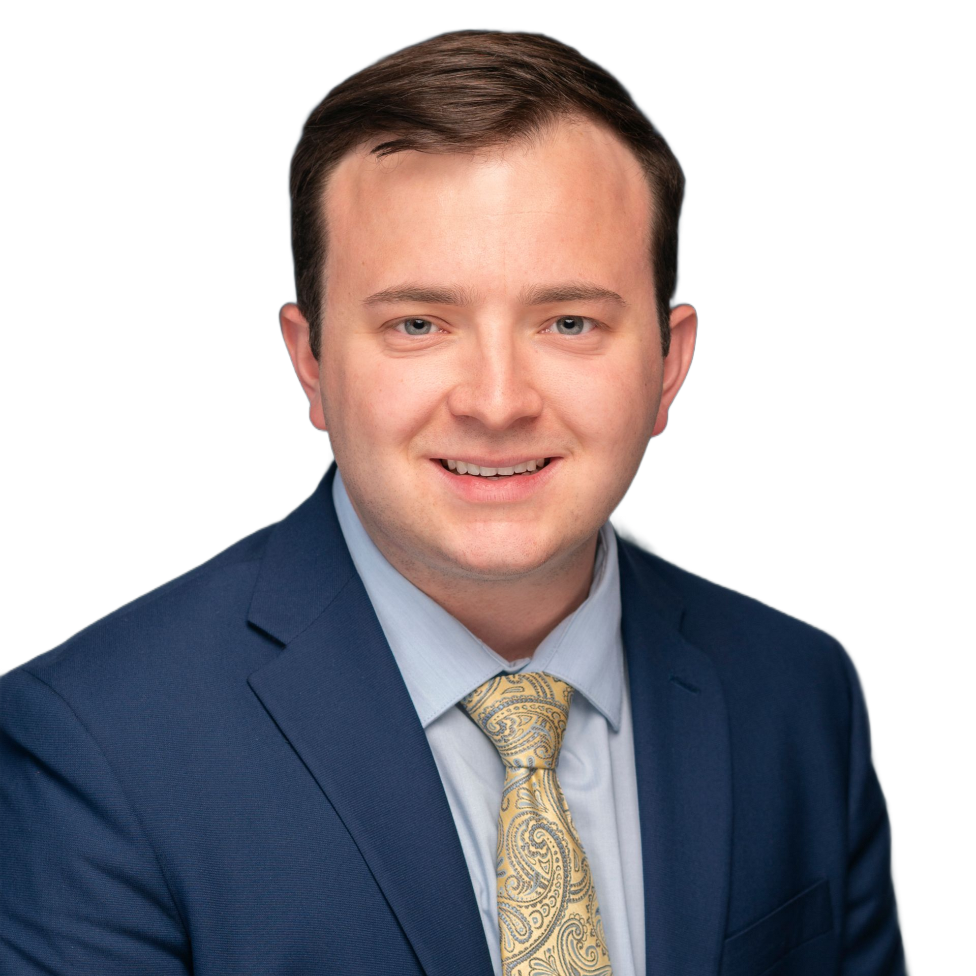 Man in a navy suit and yellow patterned tie smiles at the camera. White background.