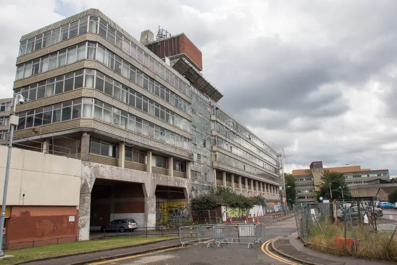 Large gray office building with curving road and cloudy sky in an urban area