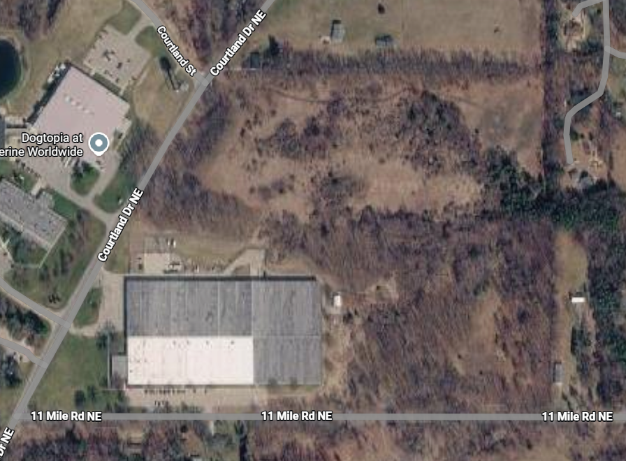 Satellite view of a rural roadside lot with woods, a large building, and nearby houses