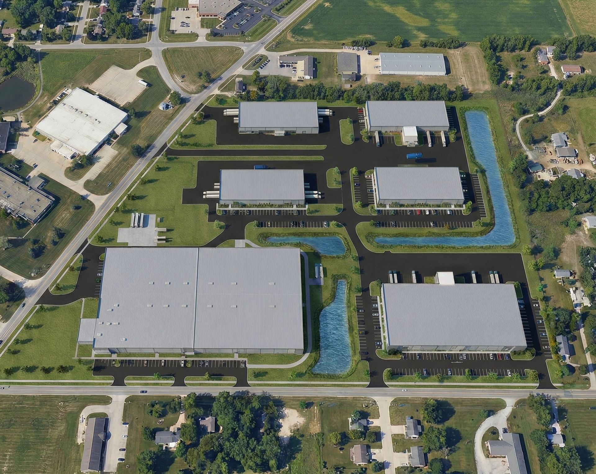 Aerial view of a facility with large gray-roofed buildings, roads, and surrounding fields.