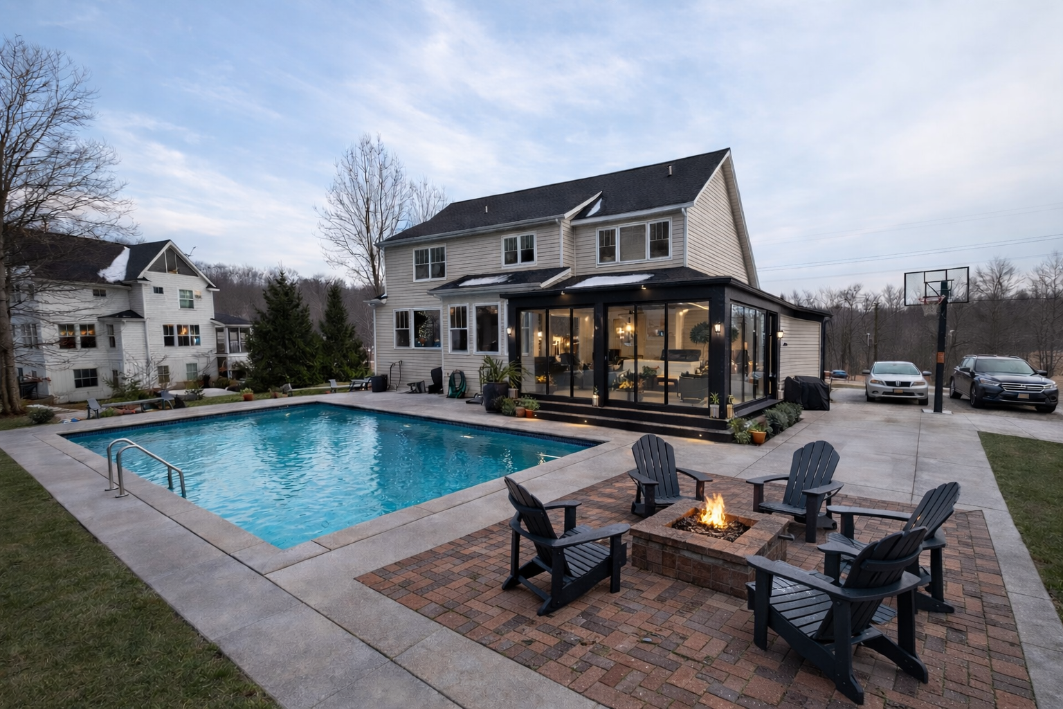 Modern house with a pool, patio seating, and a fire pit at dusk