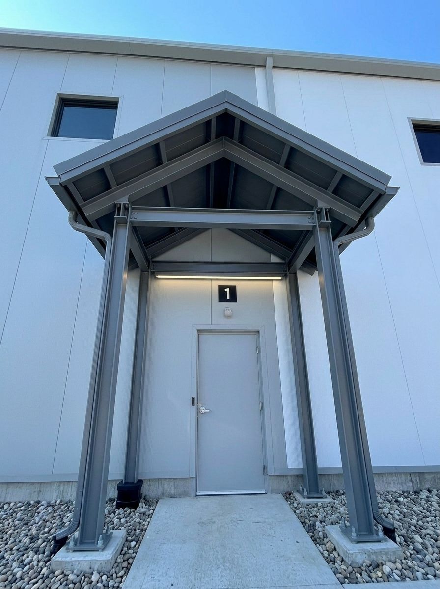 Covered entrance with gray door and metal awning on a white building