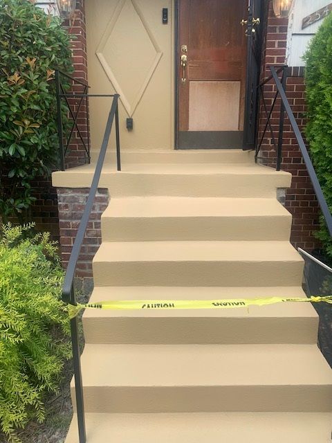 Beige front steps with black handrails leading to a house entrance, blocked by yellow caution tape