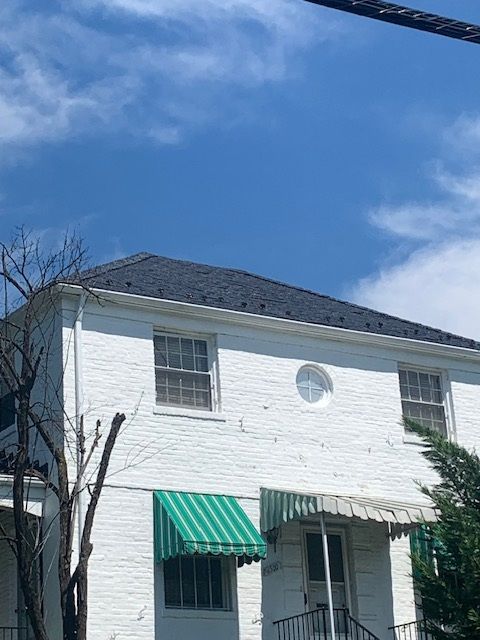 White two-story house with a dark roof and green striped awning under a blue sky