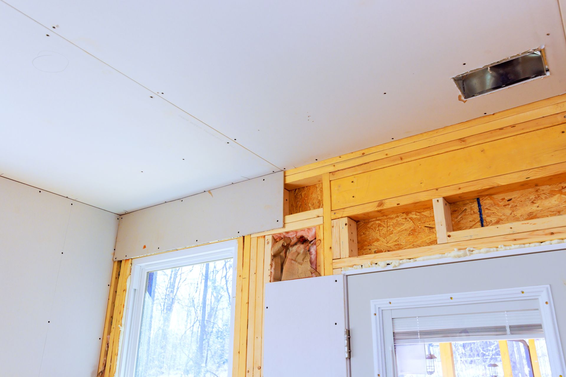 Partially finished room with white ceiling, window, and exposed wooden framing above a doorway