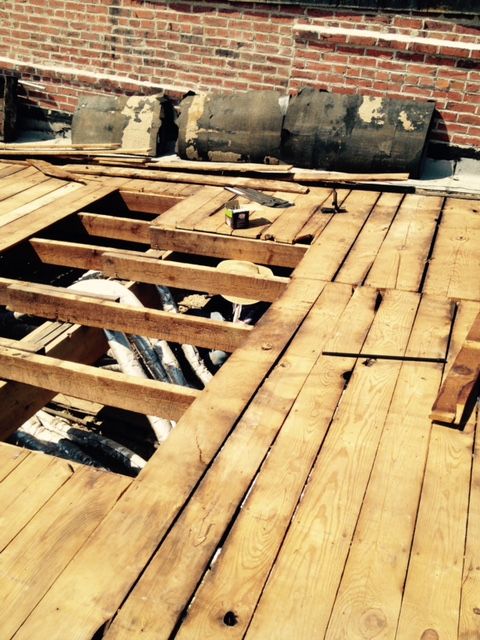 Damaged wooden floor with large missing sections beside a brick wall