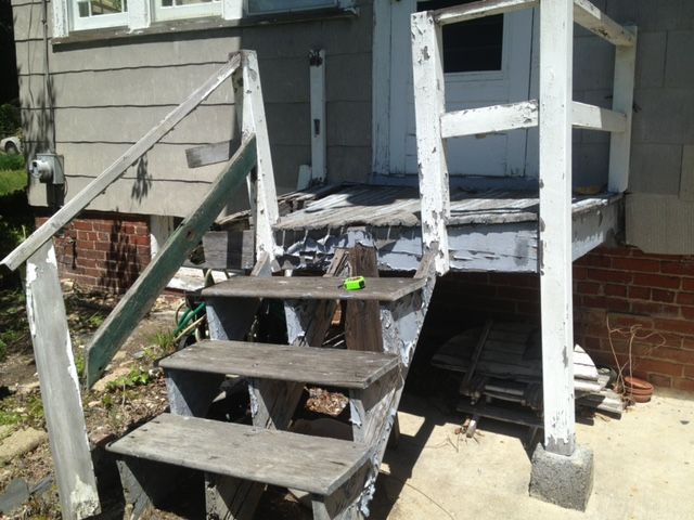 Weathered wooden steps leading to a small porch with a white door and siding on a house exterior.