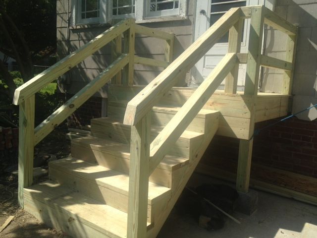 Wooden outdoor steps with railings leading to a raised porch beside a house