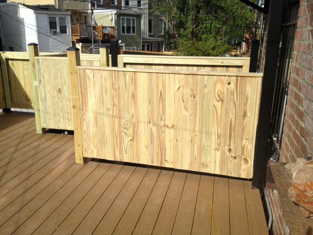 Wooden privacy fence panels on a deck beside a brick wall, with houses visible in the background
