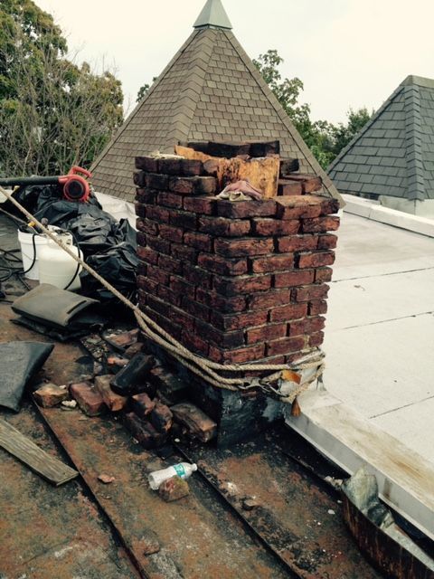 Damaged brick chimney on a rooftop with debris and exposed roof surface