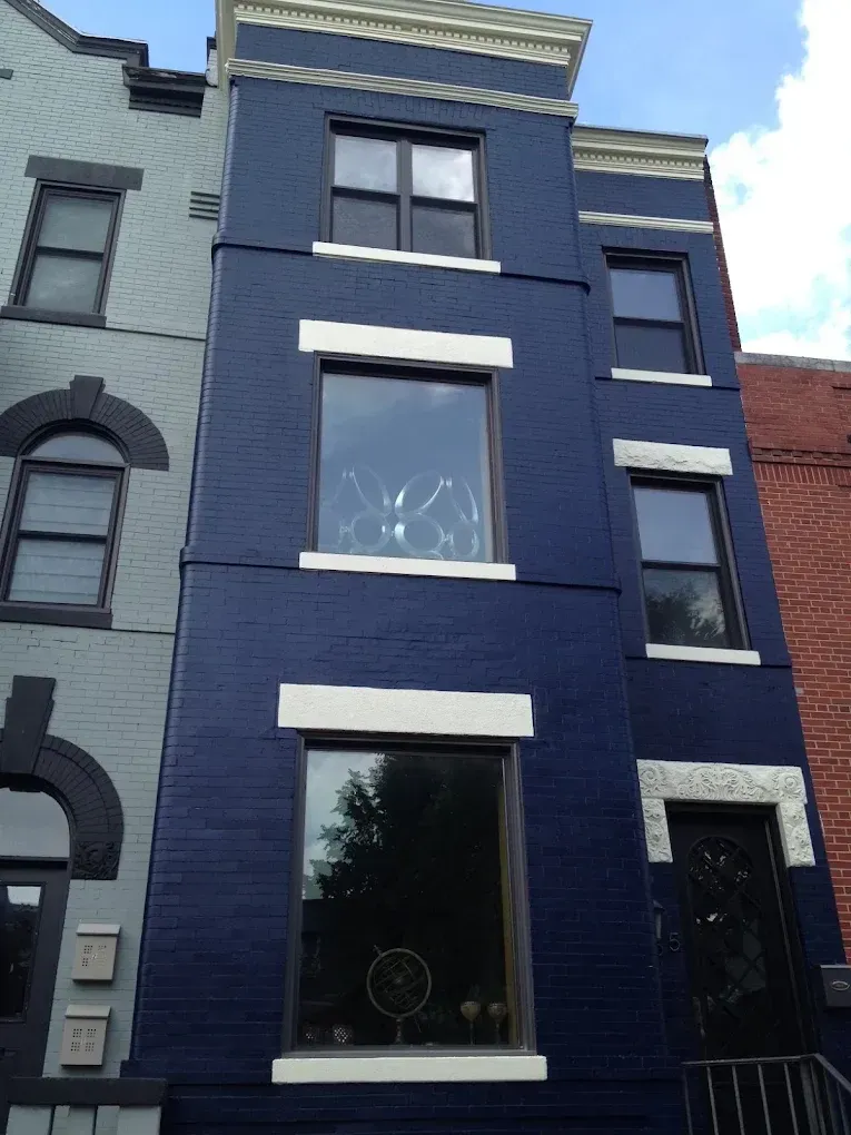 Narrow navy-blue townhouse facade with white trim and large windows on a city street