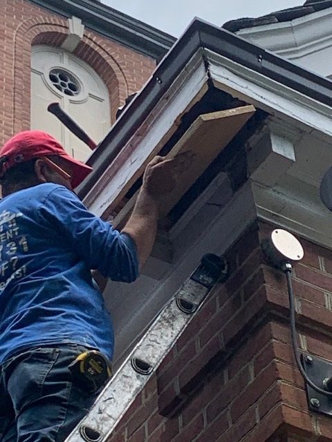 Worker on a ladder repairing roof trim on a brick building