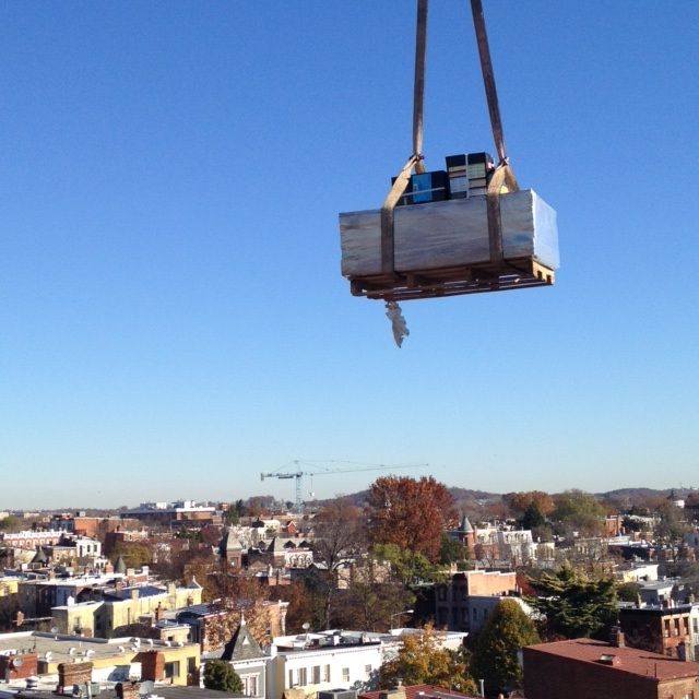 A crane lifts a pallet over a city neighborhood under a clear blue sky.