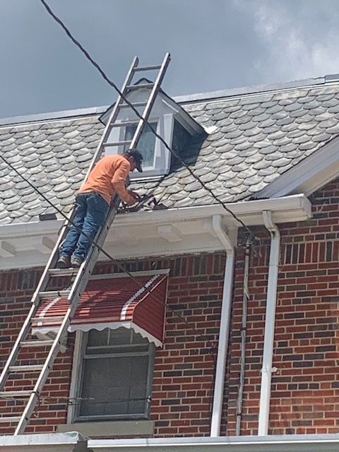 Worker on a ladder repairing a roof dormer on a brick house