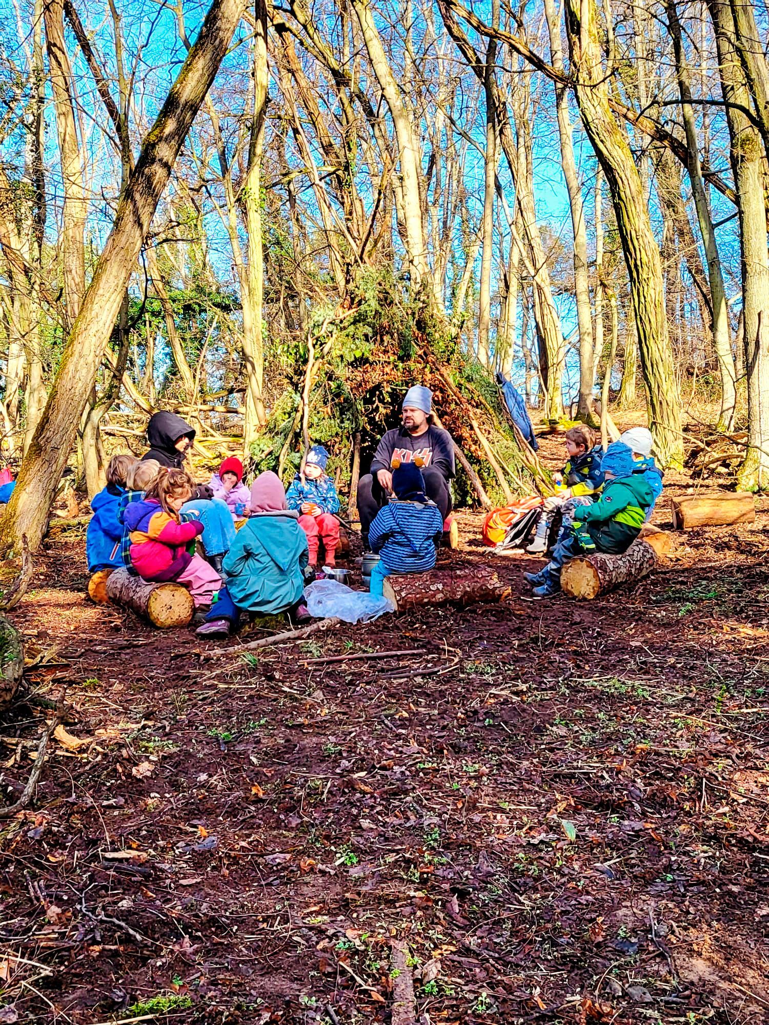 Kindergartenkinder sitzen im Kreis im Wald zusammen