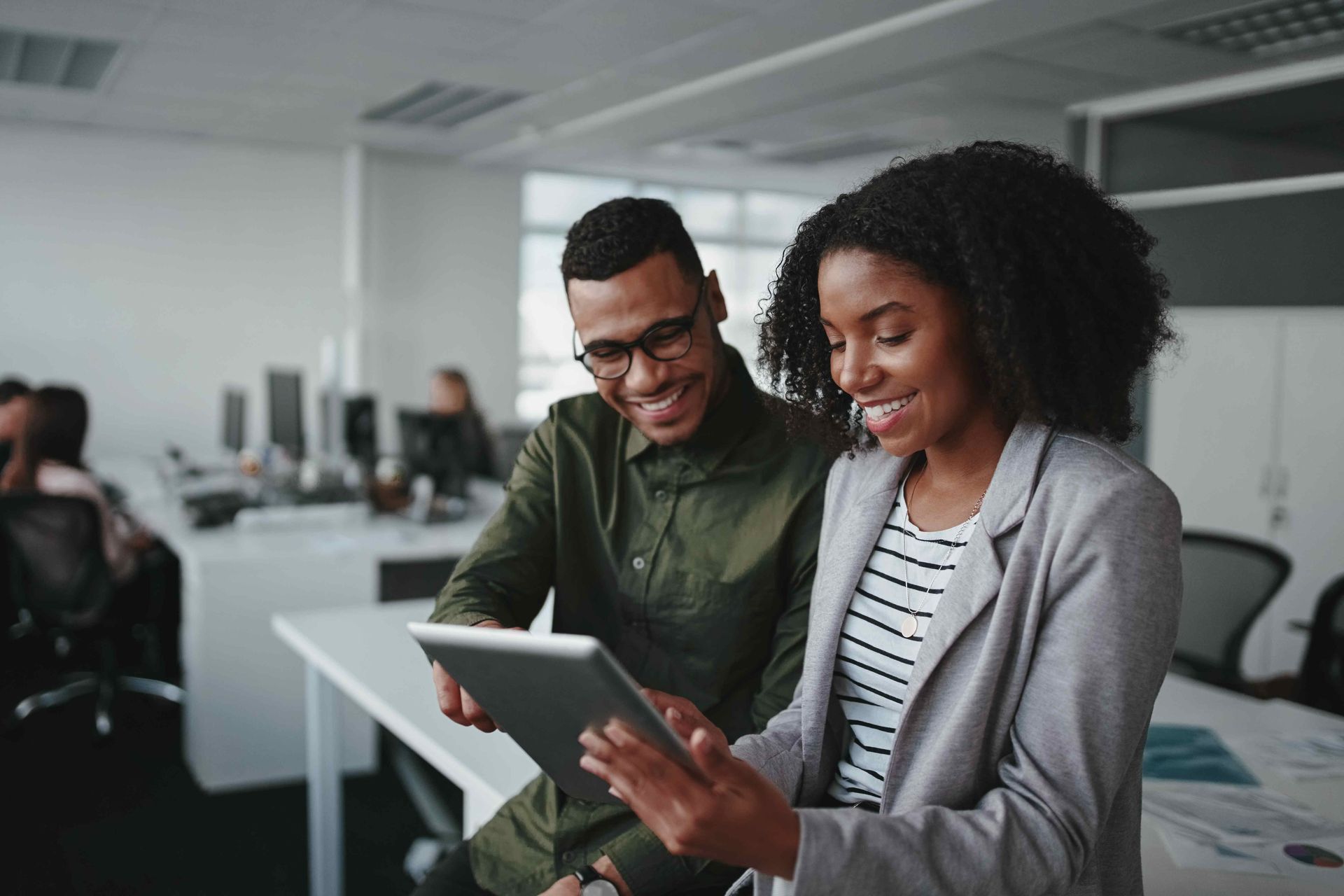 a man and a woman are looking at a tablet in an office