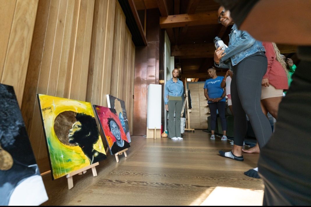 A group of people are looking at paintings on easels in a room.