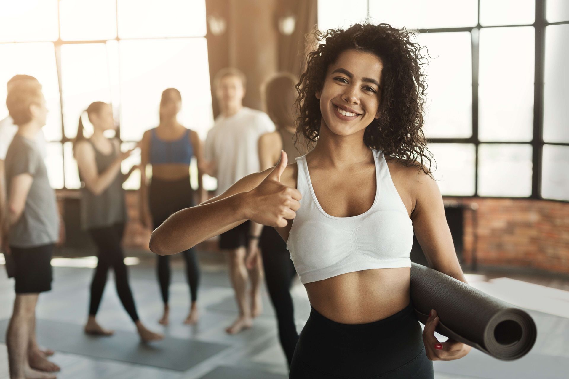 a woman is holding a yoga mat and giving a thumbs up